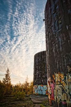 Old, rusted industrial constructions near bushes with beautiful sky