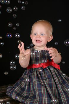 Cute blond toddler girl surrounded by bubbles sitting on a wooden trunk