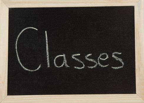 A black board with a wooden frame and the word 'CLASSES' written in chalk.