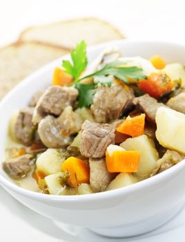 Bowl of hearty beef stew with vegetables served with rye bread