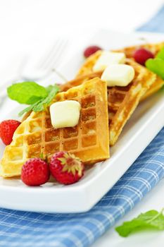 Plate of belgian waffles with fresh strawberries and pats of butter