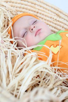 Baby dressed in a pumpkin costume sleeping in a basket