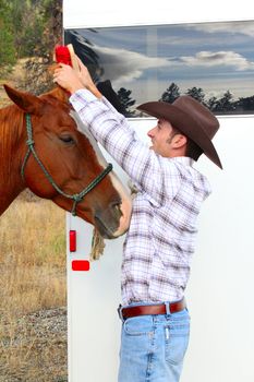 Young cowboy grooming his horse at the trailor