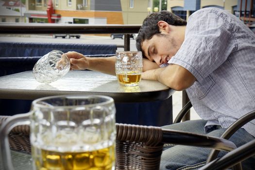 Young man passed out drunk with beer bocks on the glass table of an outdoor terrace: perfect for alcoholism, student hazing, beer binging and other related concepts.