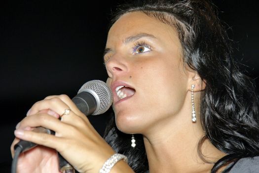 Beautiful, talented and hopeful young woman singing with emotion on stage at a bar or karaoke.