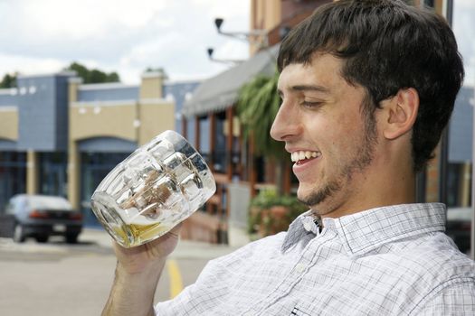 Young man or student happy to find out there is still beer in his glass while sitting outdoor on a bar's terrace during an afternoon on the town.