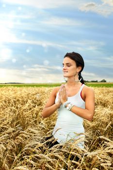 Beautiful healthy young woman connecting with nature by doing yoga and medidating at dawn in a ripe wheat field.