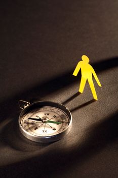 Orientation concept. Yellow paper man standing near vintage compass under beam of light on dark background