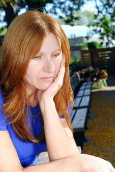 Mature woman looking sad and depressed sitting alone on a park bench