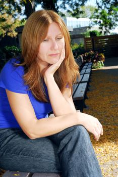Mature woman looking sad and stressed sitting on a park bench