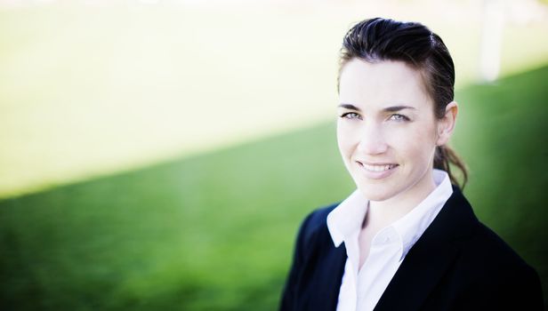 businesswoman smiling while wearing a business suit standing outside in the grass and sunshine