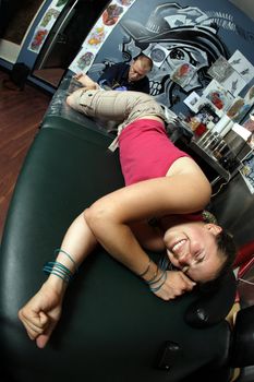 A tattoo artist applying his craft onto the lower leg of a pain-inflicted female. (Property release supplied includes tattooists' wall mural and drawings posted on the walls behind him.)
