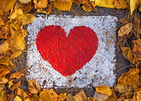 Red heart painted on the road in a dry leaves frame