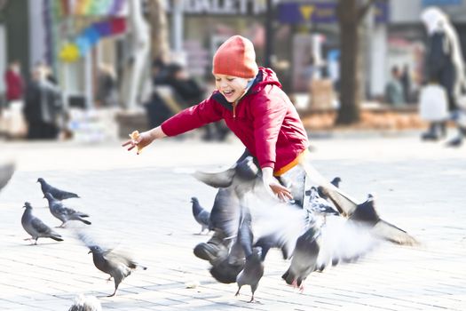 Happy kid playing with pigeons in a city park