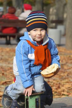 Cheerful boy with the bread in his hand playing in autumn park