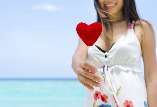 Portrait of a smiling young woman holding a heart shape at beach