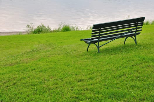 Empty bench on green grass by river