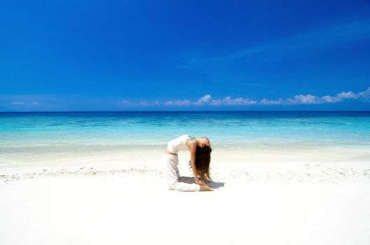 Woman practicing Yoga(Camel Pose) on the beach.