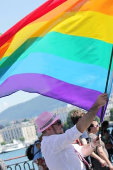 Man holding a big rainbow flag while taking part in Gay Pride Parade, Geneva, Switzerland.