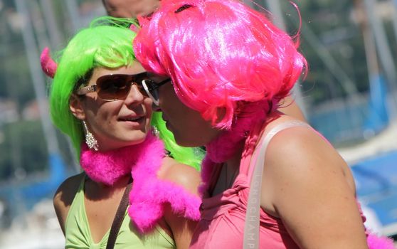 Two unidentified women wearing colored wigs and glasses and looking at each other with love while taking part in Gay Pride Parade 2011, Geneva, Switzerland.