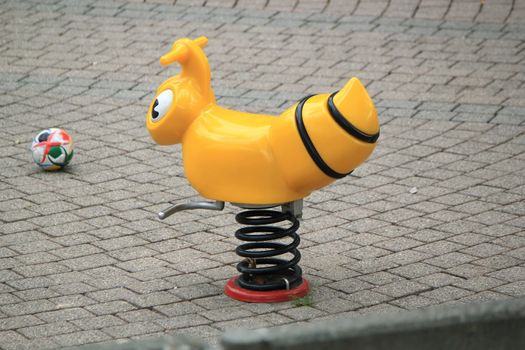Playground for children with one yellow plastic animal on springs and a colored ball on the ground