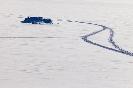 Pattern of snowmobil tracks in otherwise untouched fresh powder snow surface with rocky outcrop.