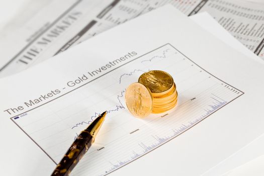 Gold Eagle one ounce coins stacked into graph of gold on business pages of newspaper with graphs showing drop in prices