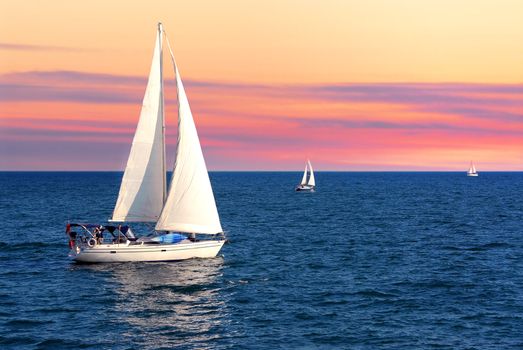 Sailboat sailing towards sunset on a calm evening