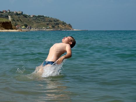 Young boy jumping into wave on a sunny beach