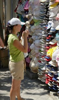 Young woman selects cap on the market.