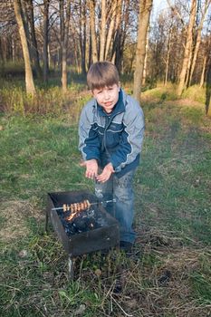 Small boy lights bonfire on the forest clearing