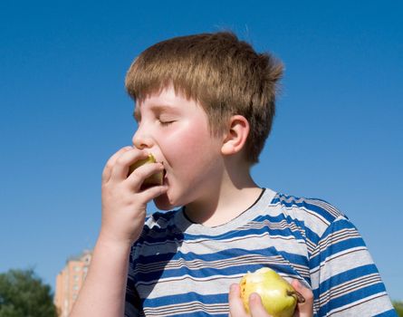 Boy eats apple with blue sky at background