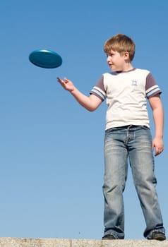 A little boy throws a flying disk with sky at background