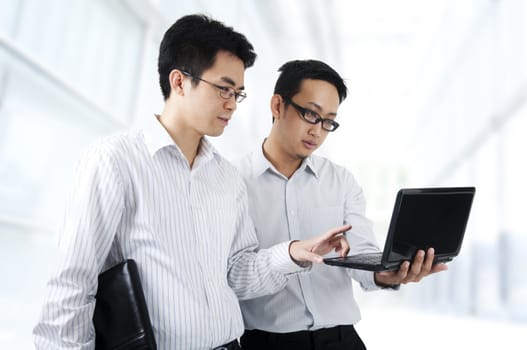 Two Asian young executives working on laptop, office building as background