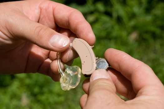 Changing a digital hearing aid battery. The battery is in the opened battery-cover.