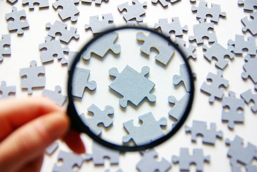 Hand with magnifying glass and puzzle isolated on white background