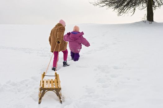 Two children climb up on a hill with a yellow sledge.