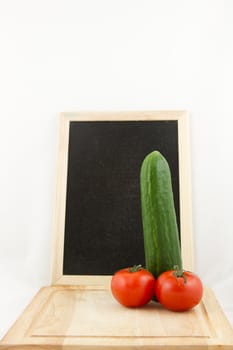 A chopping board with phallic salad, cucumber and tomato, with a chalk board in the background all on white.