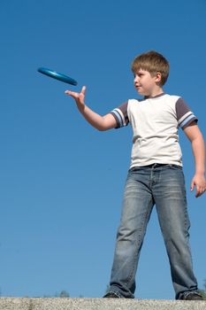 A little boy throws a flying disk with sky at background