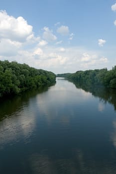 Summer. River. Blue sky and green trees are reflected in water.