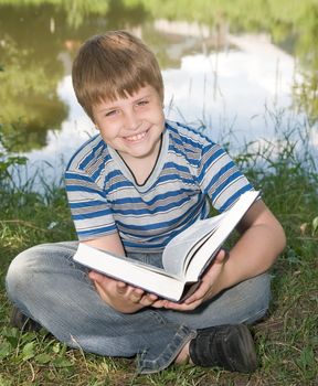 A little boy reads a big book with river at background