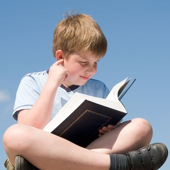 A little boy reads a big book with sky at background