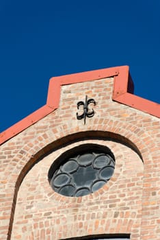 Rose window and a cast iron fixture of a brick factory house on polarised deep blue sky.
