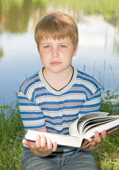 A little boy reads a big book with river at background