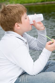 little boy drinks milkshake on a riverside