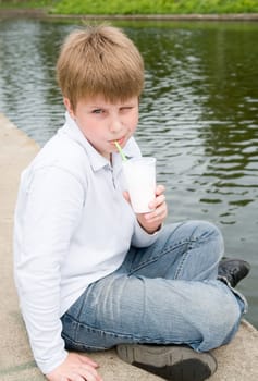 little boy drinks milkshake on a riverside