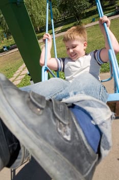 The little boy on a swing in city park