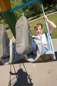 The little boy on a swing in city park