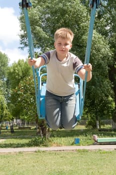The little boy on a swing in city park