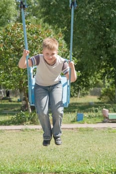 The little boy on a swing in city park